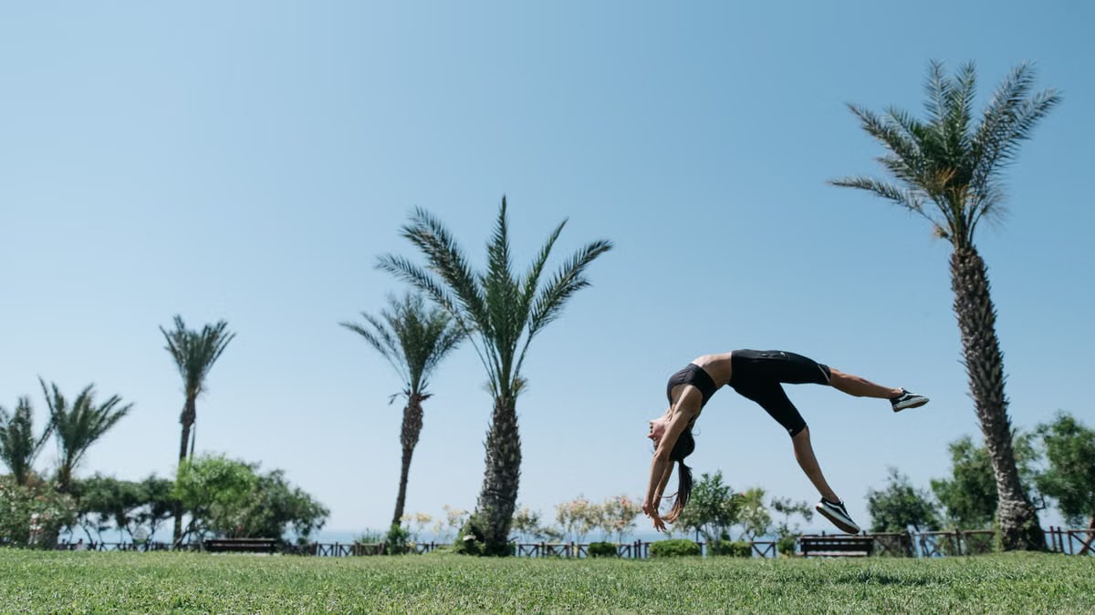 Athletic woman executing a backflip amidst palm trees in a sunny outdoor park.